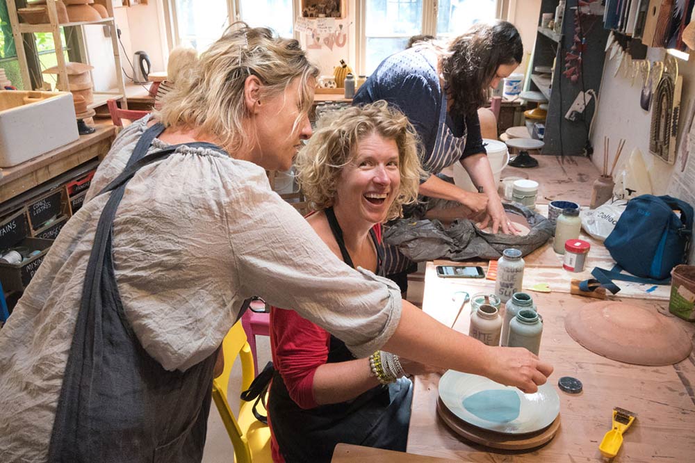 Image of jane demonstrating ceramics and pottery techniques to a laughing student